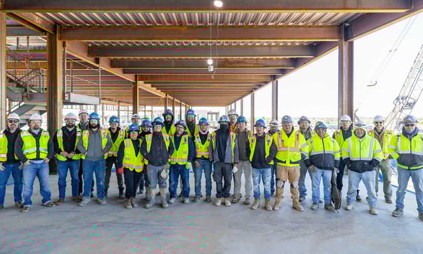 A group of construction workers smiling and posing together for a photo at a construction site