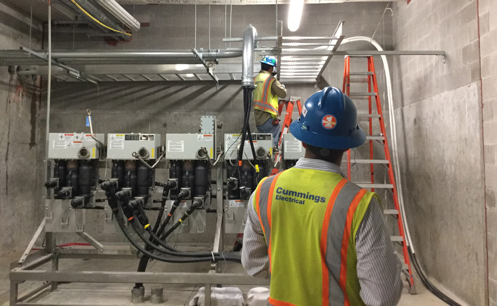 two construction workers wearing hard hats working on a large electrical system