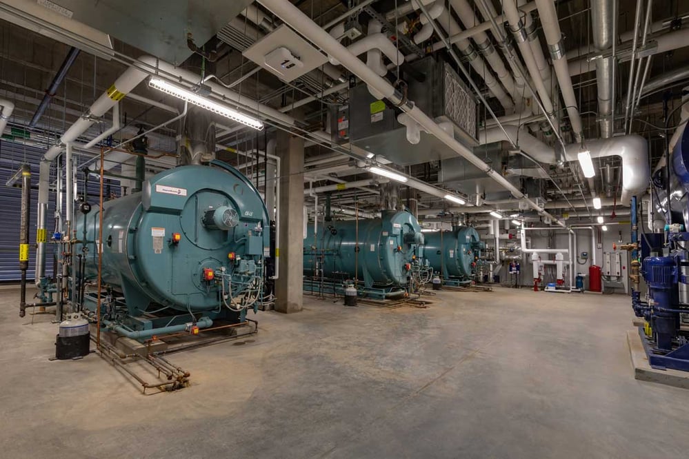 Large medical boiler room with various labeled piping and conduit