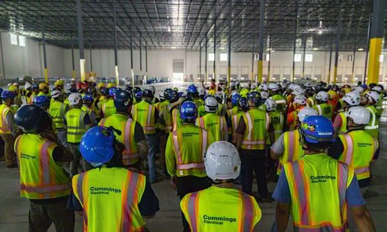 A group of individuals wearing hard hats and safety vests, engaged in a construction or safety-related activity indoors