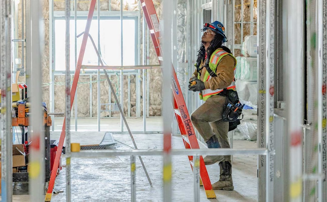a man with PPE climbing a ladder in a room under construction