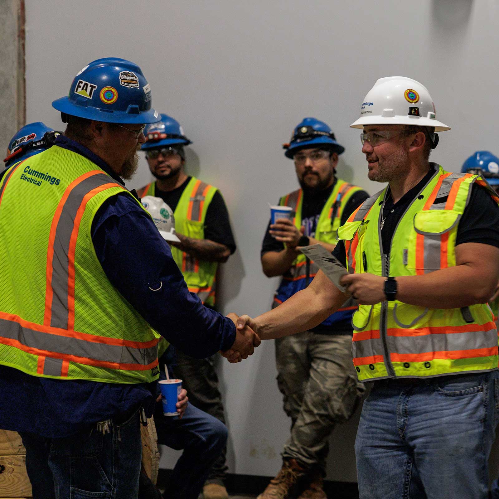 A group of men in hard hats and safety vests shaking hands at a construction site