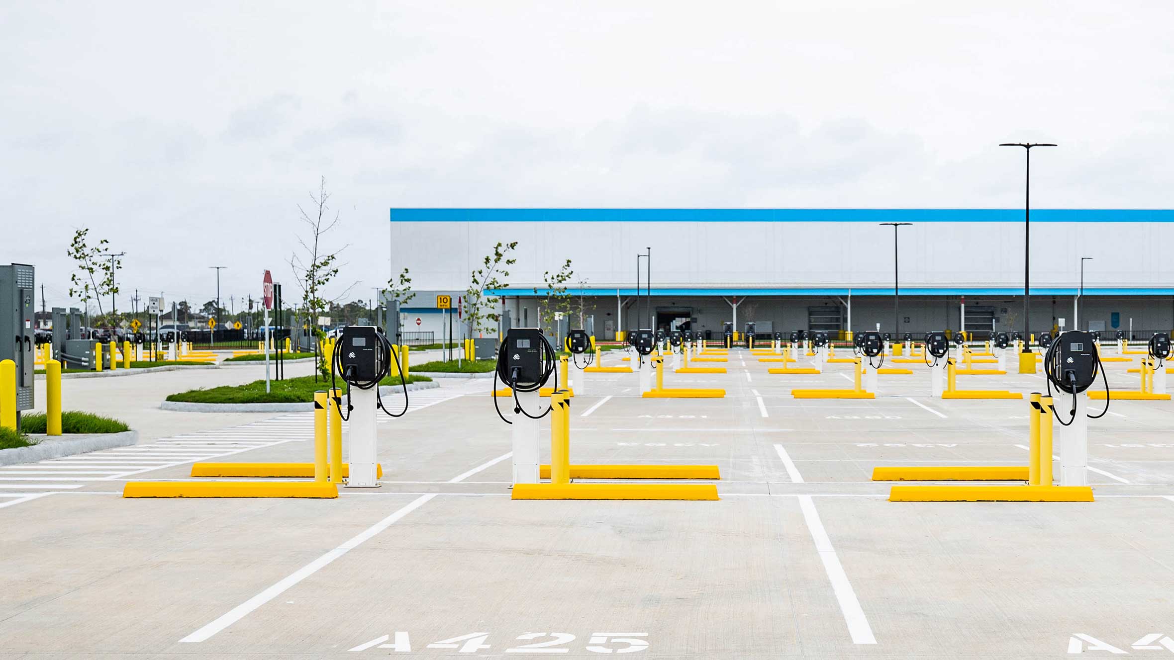 A parking lot featuring yellow poles, blue lines, and an EV charging station for electric vehicles