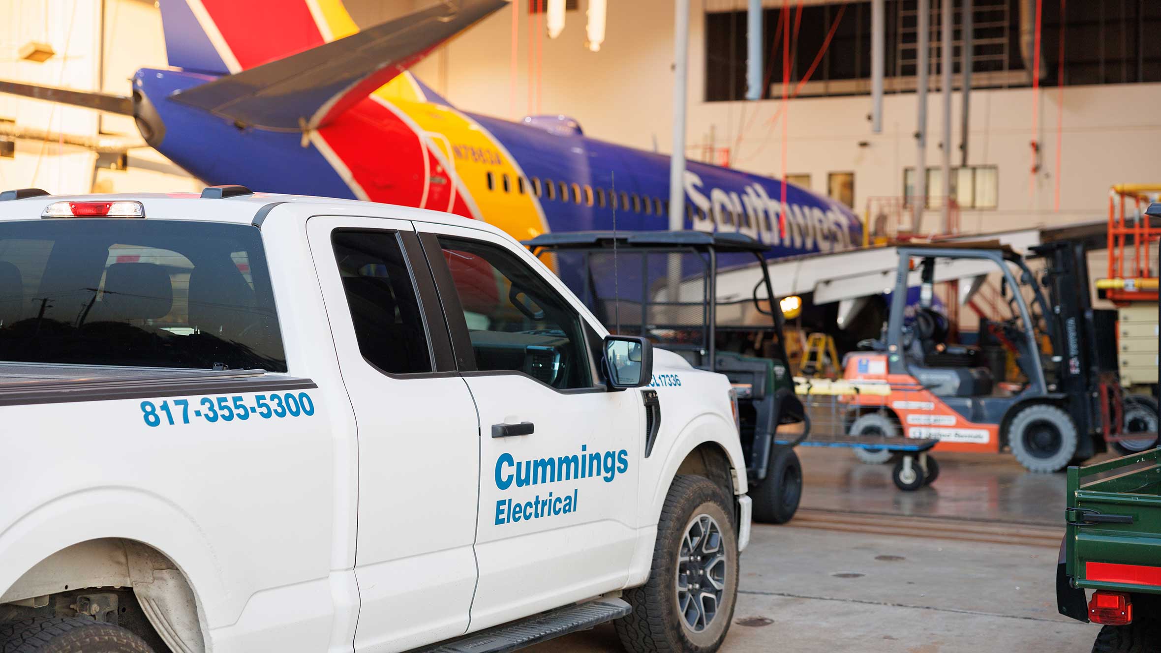 A white truck is parked in a spacious hangar garage, surrounded by concrete walls and large hangar doors