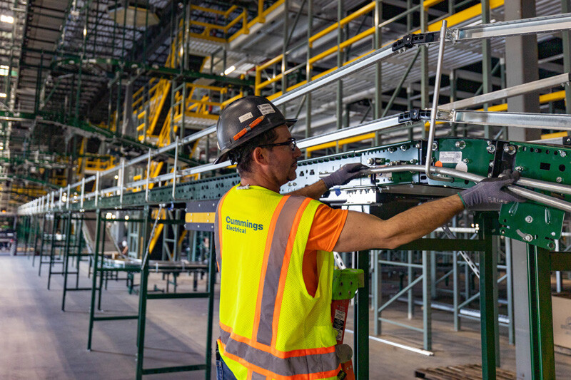 electrician wearing a hard hat and a vest maneuvering pipes