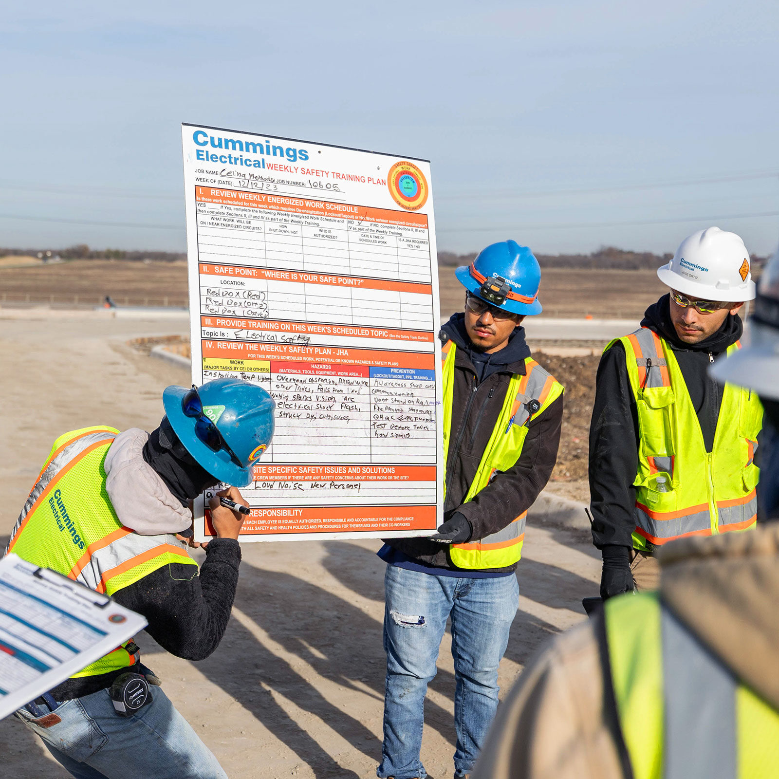 A construction crew in safety gear reviews a weekly safety training plan outdoors