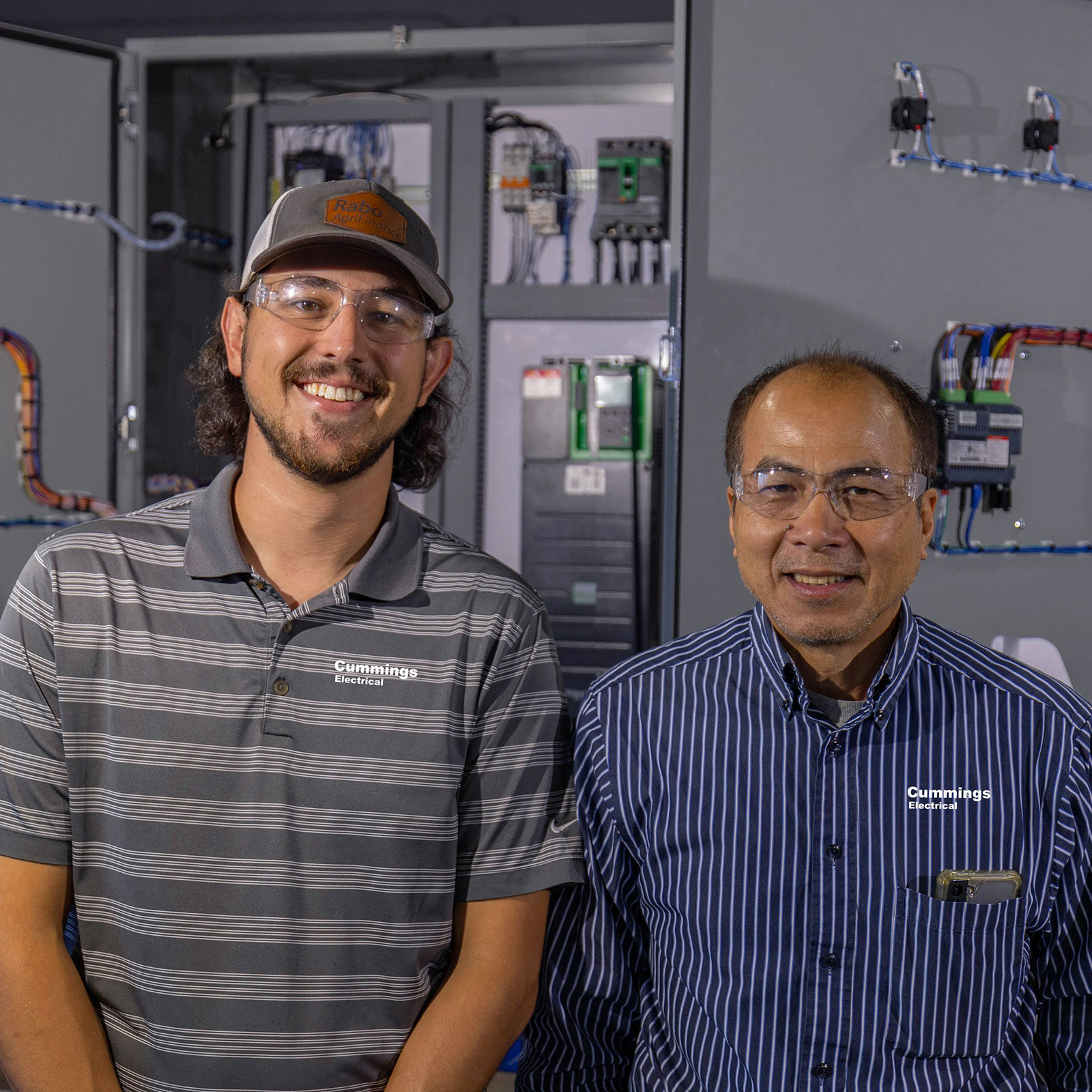 Cummings Electrical team smiling with a panel behind them