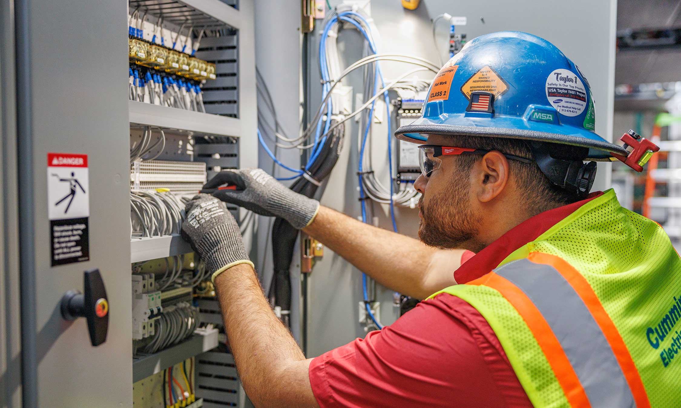Electrician using a hard hat and a safety vest working on a panel