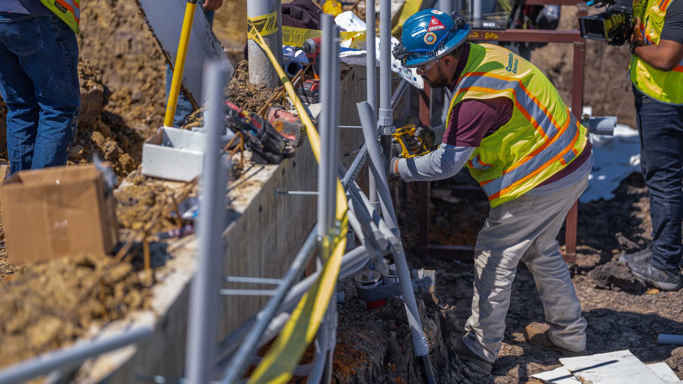 a man with protective gear working on a row of conduit in the dirt