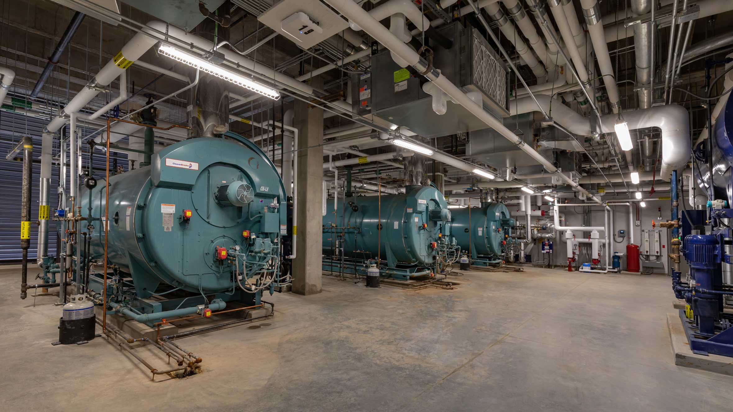 A hospital utility room with large conduits on the ceiling and backup power systems