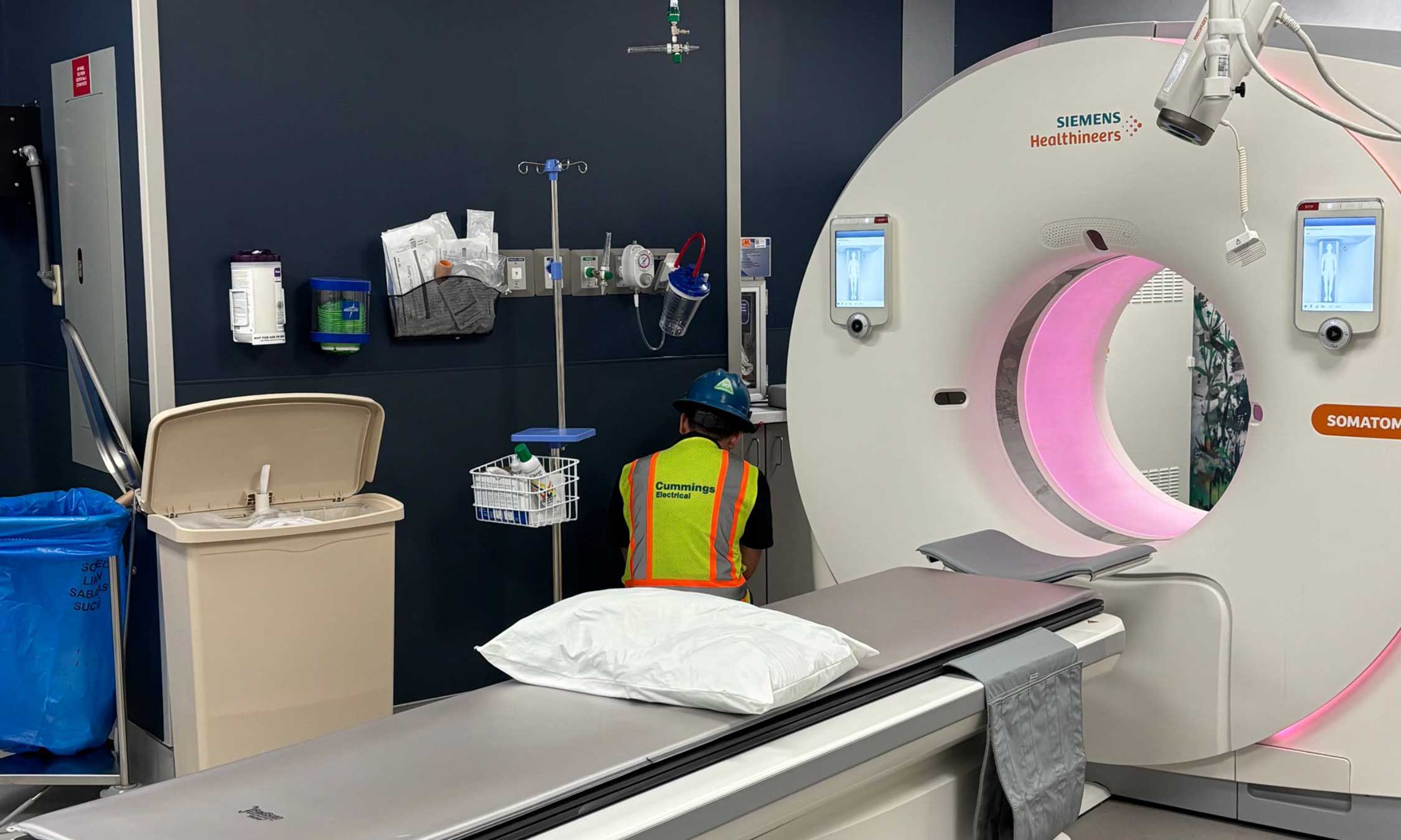 Technician in safety gear finalizing work on a CT scanner in a completed diagnostic imaging room