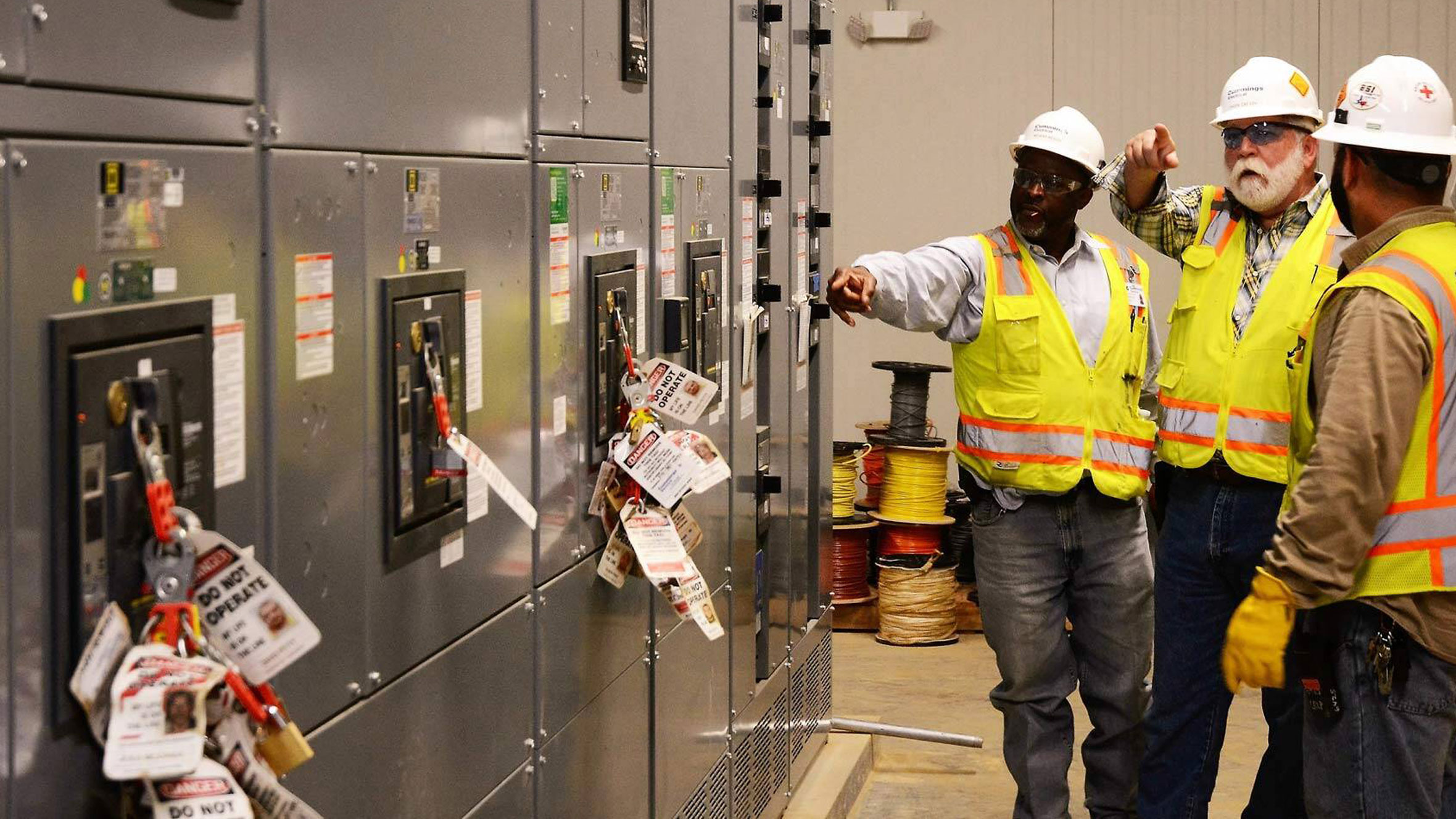 3 men in ppe evaluating electrical panels