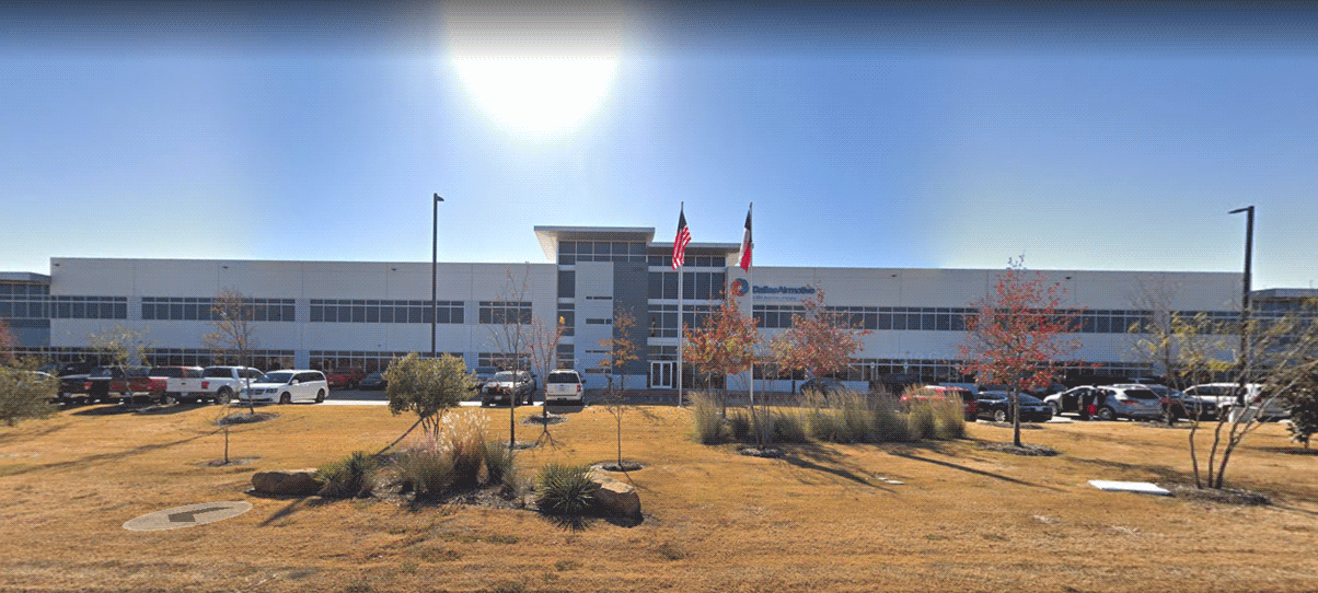 Front view of the Dallas Airmotive corporate facility with flags, vehicles, and a landscaped lawn under clear skies