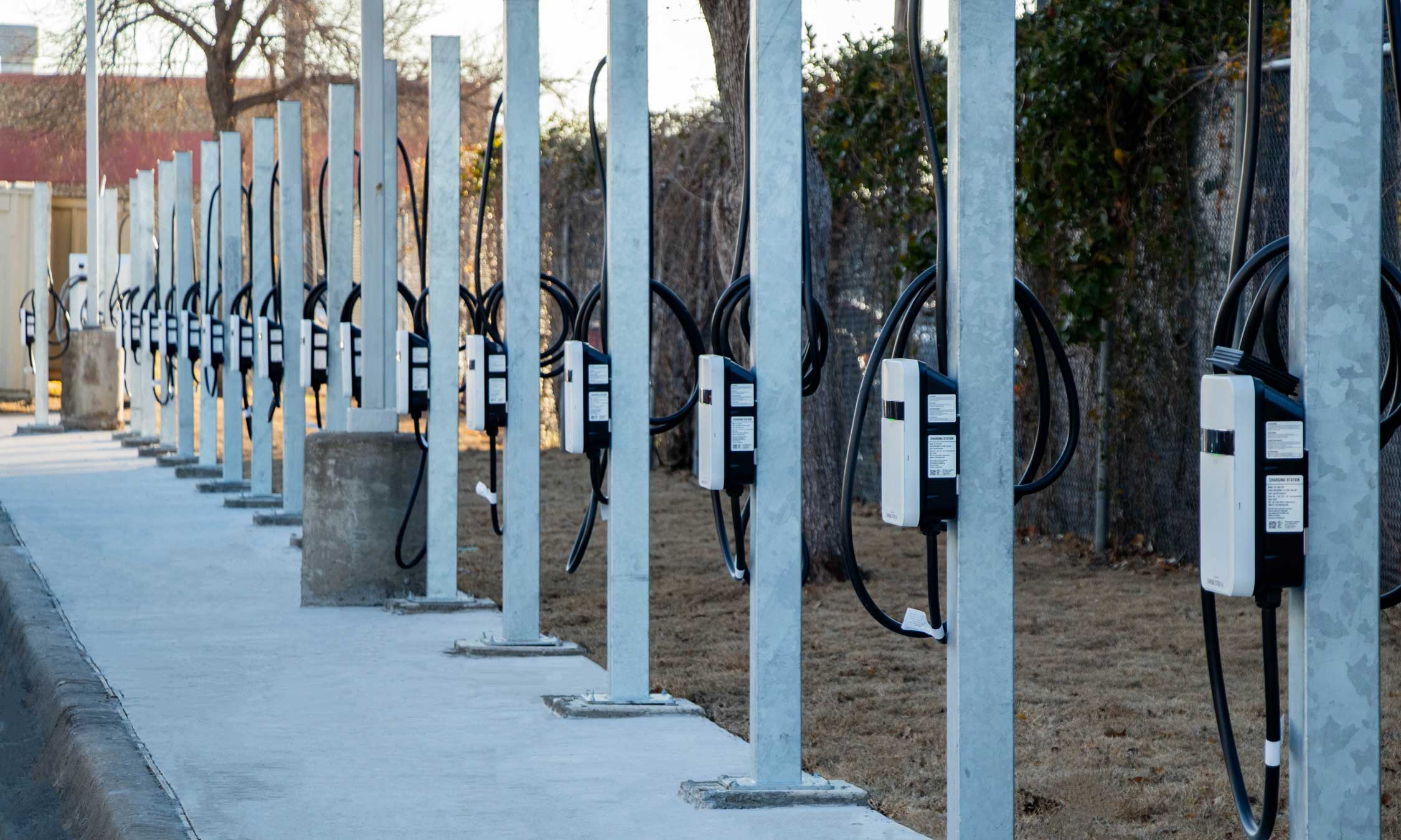 Backside view of electric vehicle chargers and cabling installed on galvanized steel posts along a sidewalk