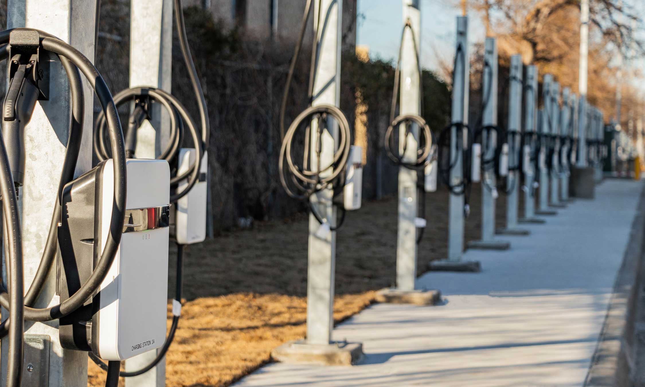 Outdoor view of a row of electric vehicle charging stations mounted on steel poles along a concrete pathway