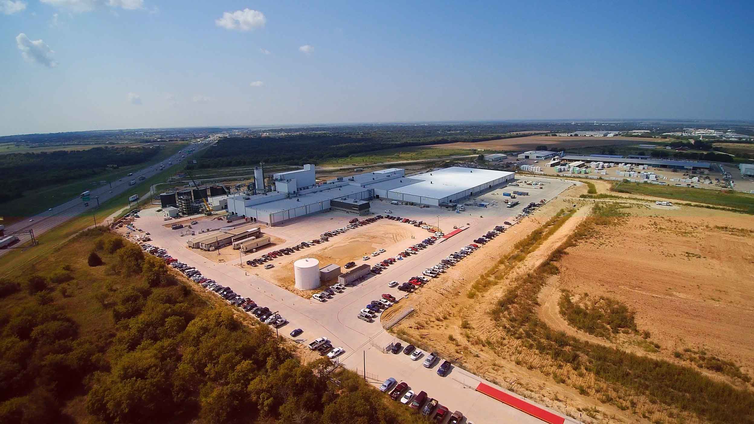 Aerial view of a remote asphalt plant surrounding by a field and a highway