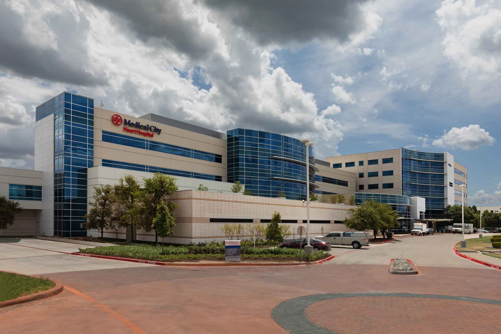 A hospital exterior view with cars parked outside and a cloudy sky