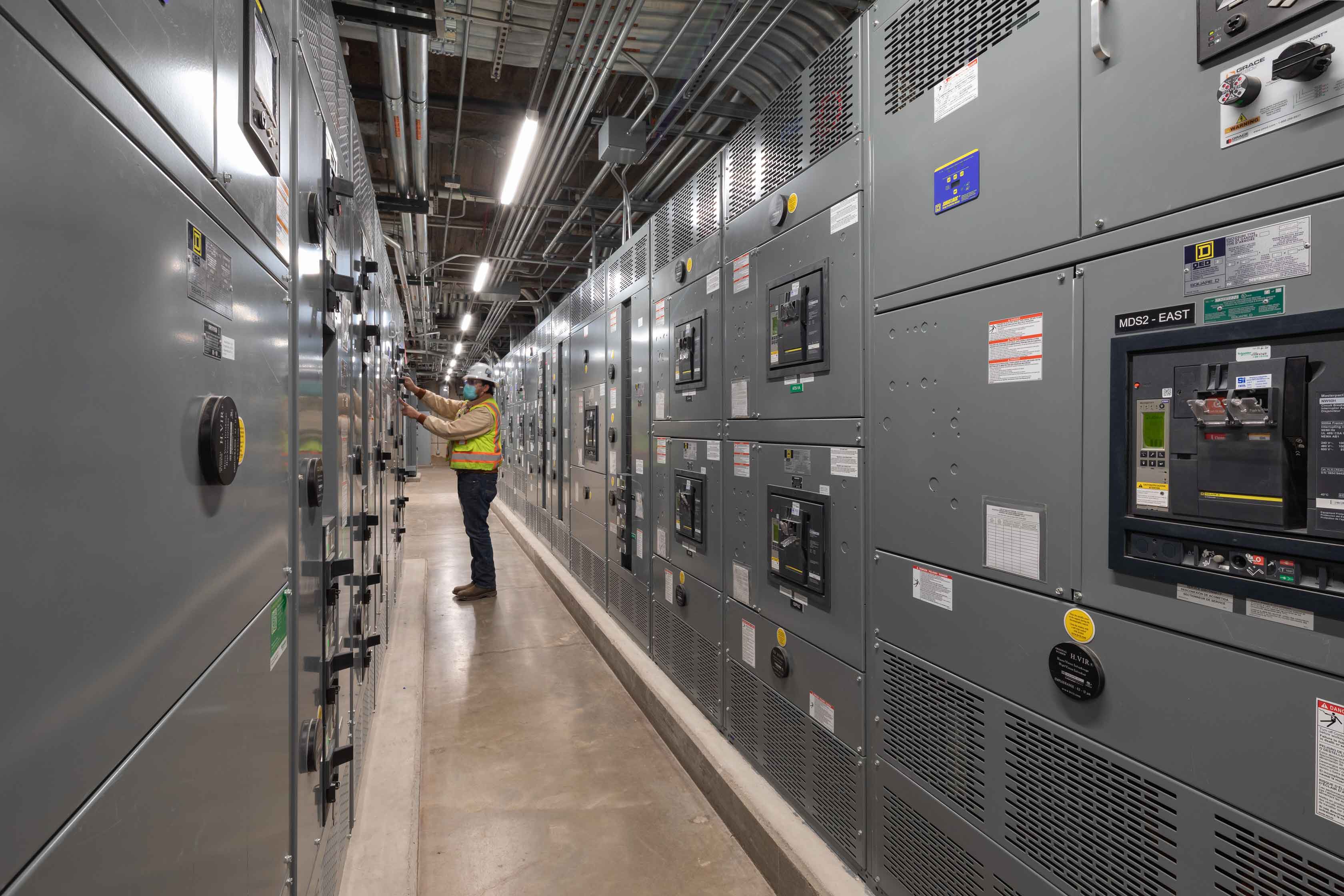 a man with protective equipment working in a row of electrical panels