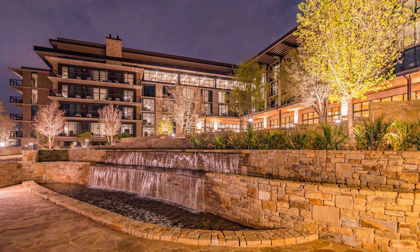 Nighttime view of a resort featuring terraced stonework, water features, and architectural lighting