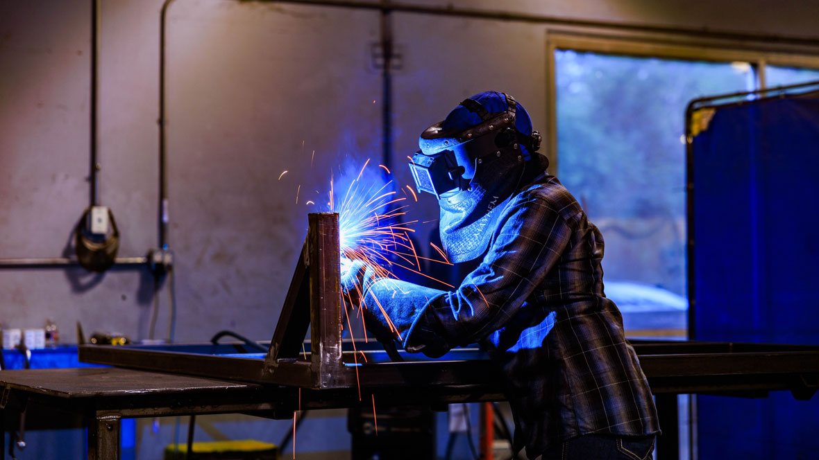 view of a professional welding with full protective gear and sparks flying out from the weld