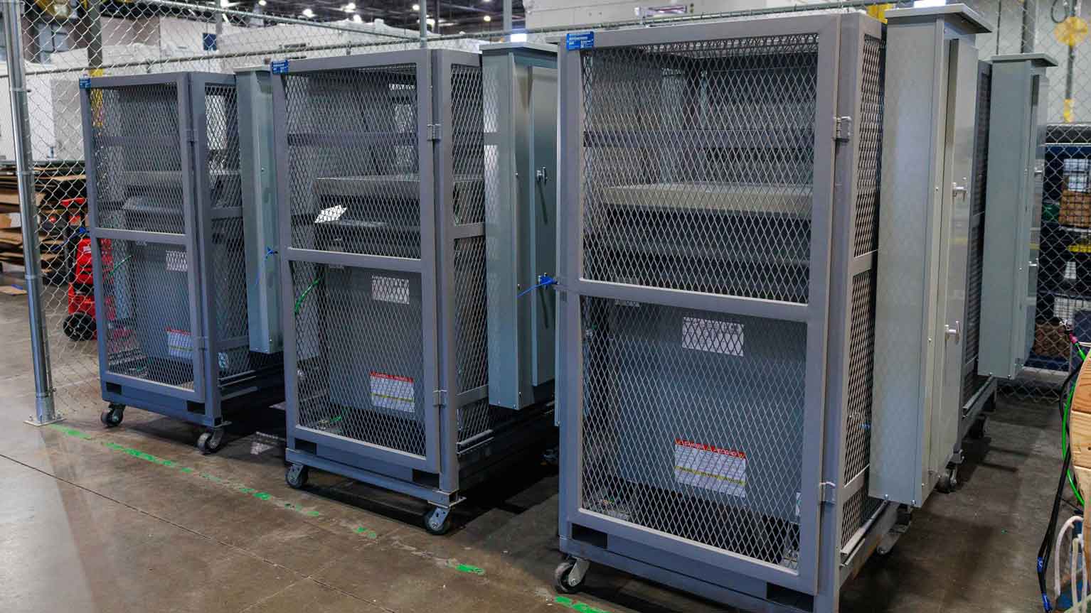 Row of electrical skids enclosed in metal mesh for secure transport and site use
