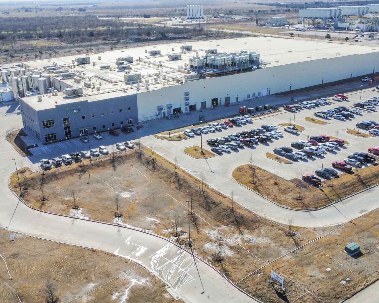 Aerial view of a large manufacturing facility with multiple cars parked in a winding parking lot
