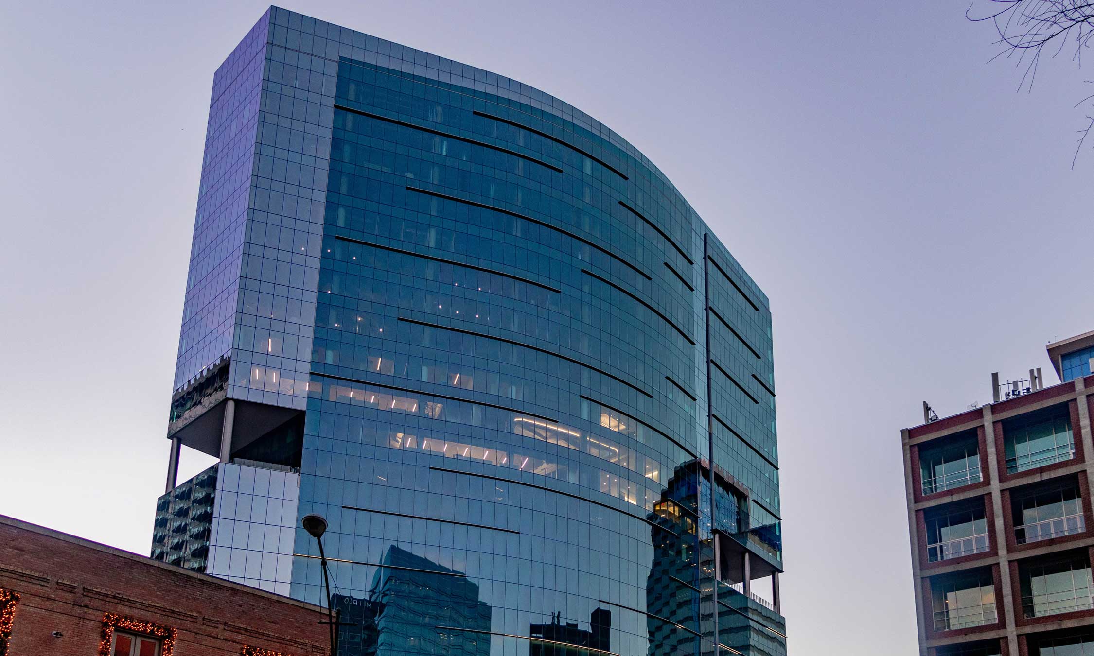 Glass high-rise building with curved architecture reflecting the city skyline during early evening light