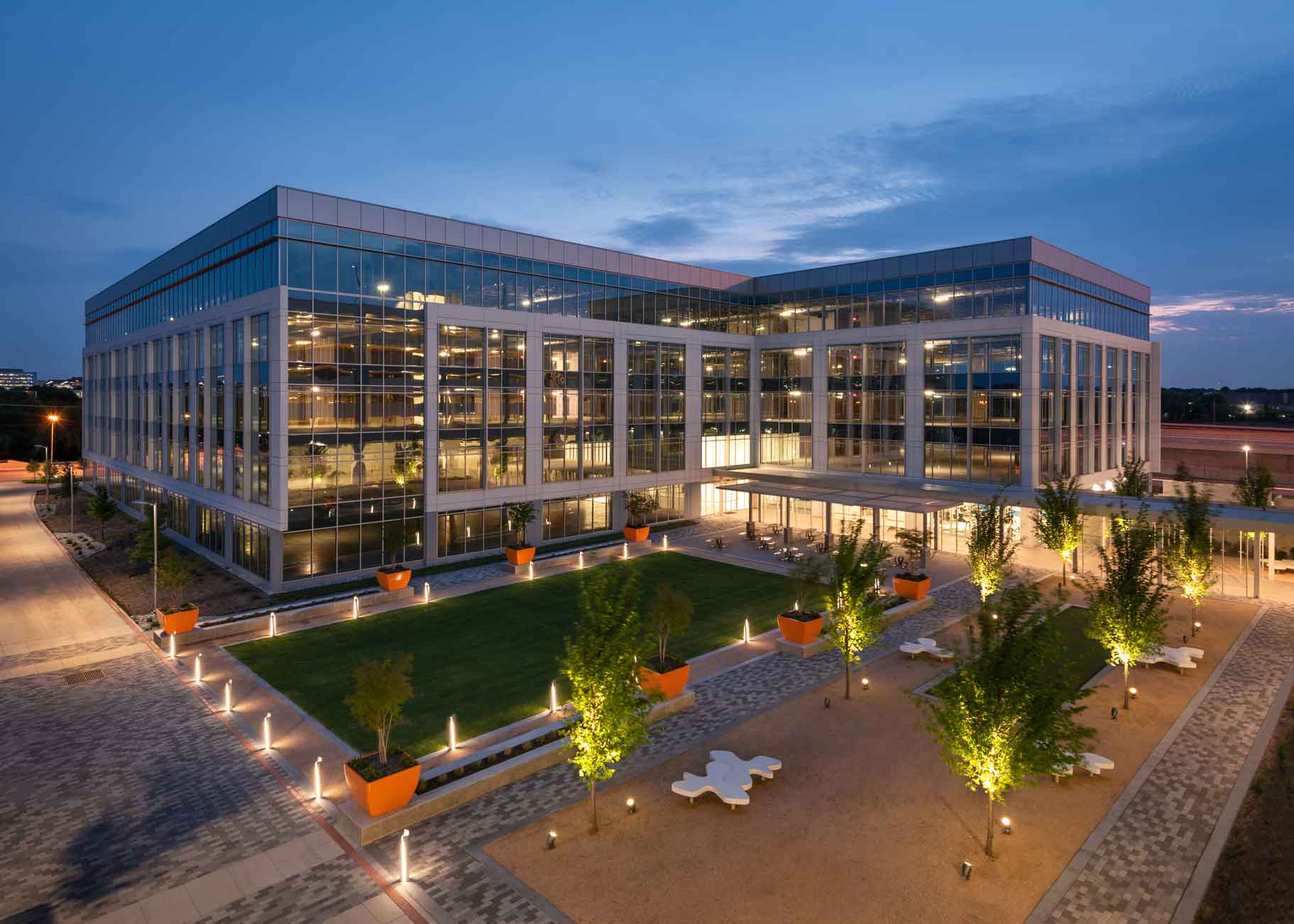 Outdoor sunset view of a contemporary office building with a green area and trees surrounding the entrance