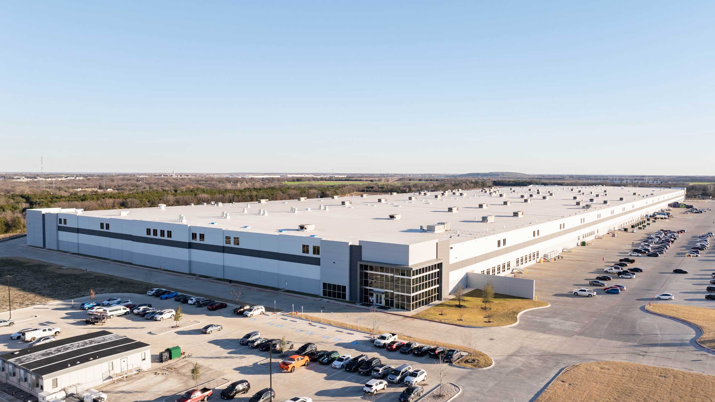 Wide view of an advanced manufacturing facility with expansive parking and multiple bays