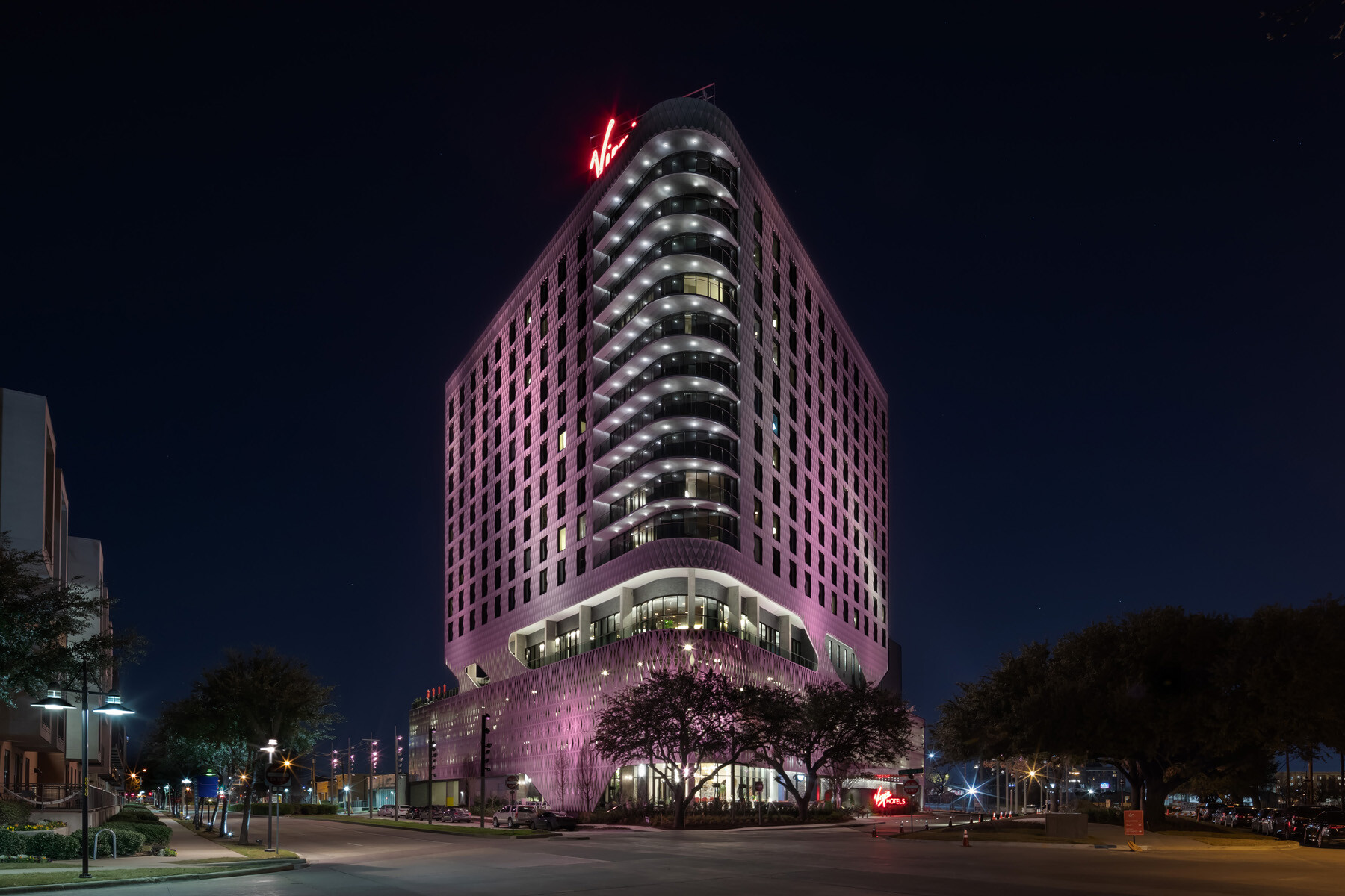 night view of the exterior of a modern hotel with red and purple lighting along the side of the building