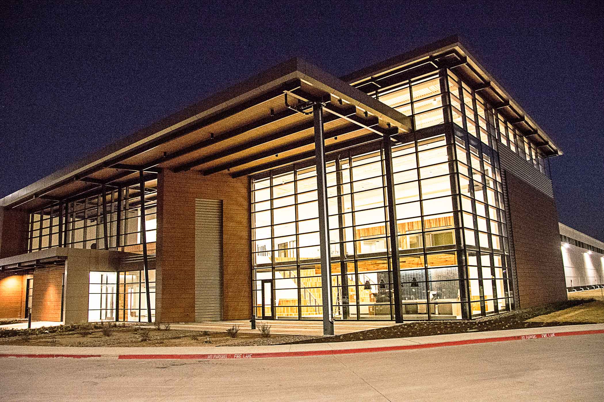 Nighttime view of a modern building with bright lighting shining through large window paneling
